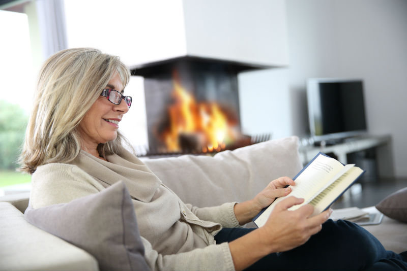 Woman reading at home beside a fireplace.