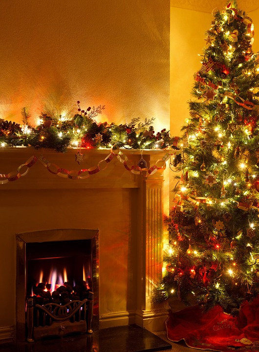 Lit Christmas tree beside a fireplace.
