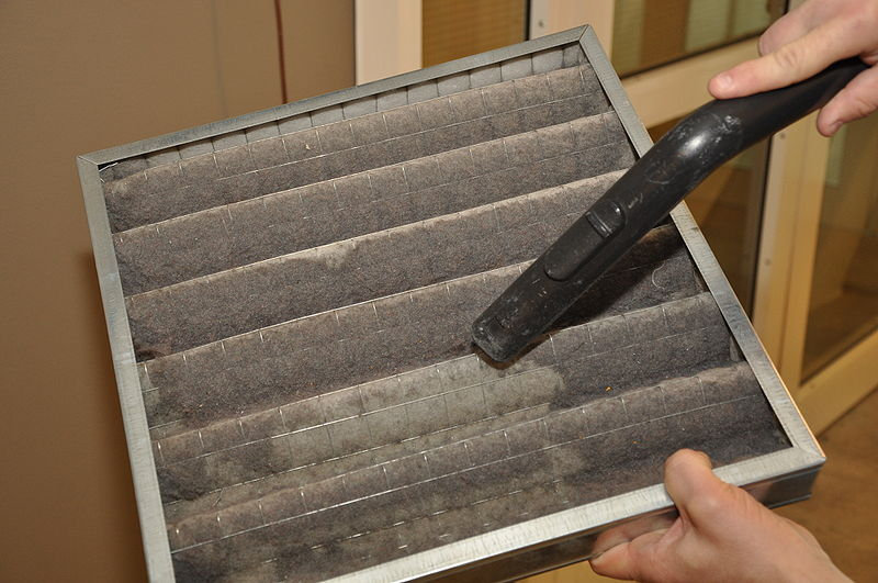 Hand vacuuming dust from a furnace filter.
