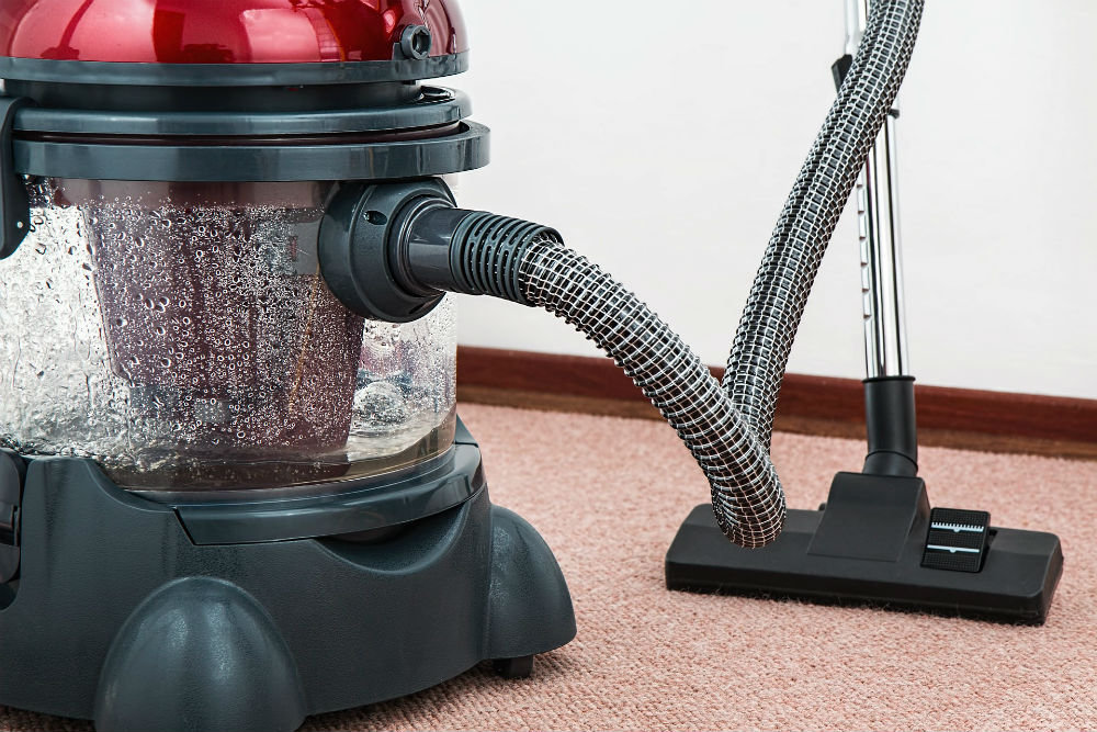Canister vacuum cleaner with hose and floor nozzle on carpet.
